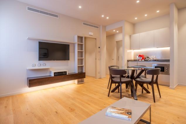 Modern living room with kitchen, glass table, and wall-mounted TV.